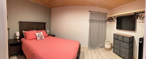 Ein Schlafzimmer mit einem Bett, einem Nachttisch, einer Kommode, einem Spiegel und einem Fenster mit Vorhängen.