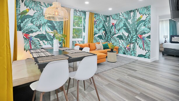 Ein modernes Wohnzimmer mit Essbereich, mit tropischem Blattentapete, einem orangefarbenen Sofa und einem Esstisch mit Stühlen.