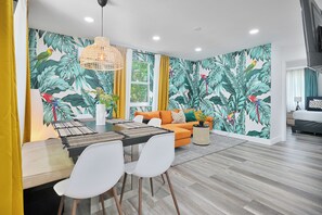 A modern living room with a dining area, featuring a tropical leaf wallpaper, an orange sofa, and a dining table with chairs. -  Jungle Getaway Wynwood Massage shower BBQ Patio (Miami)