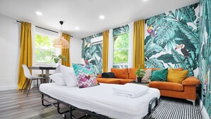 Ein modernes Hotelzimmer mit Bett, einer Couch, einem Essbereich und einer Wand im tropischen Stil.
