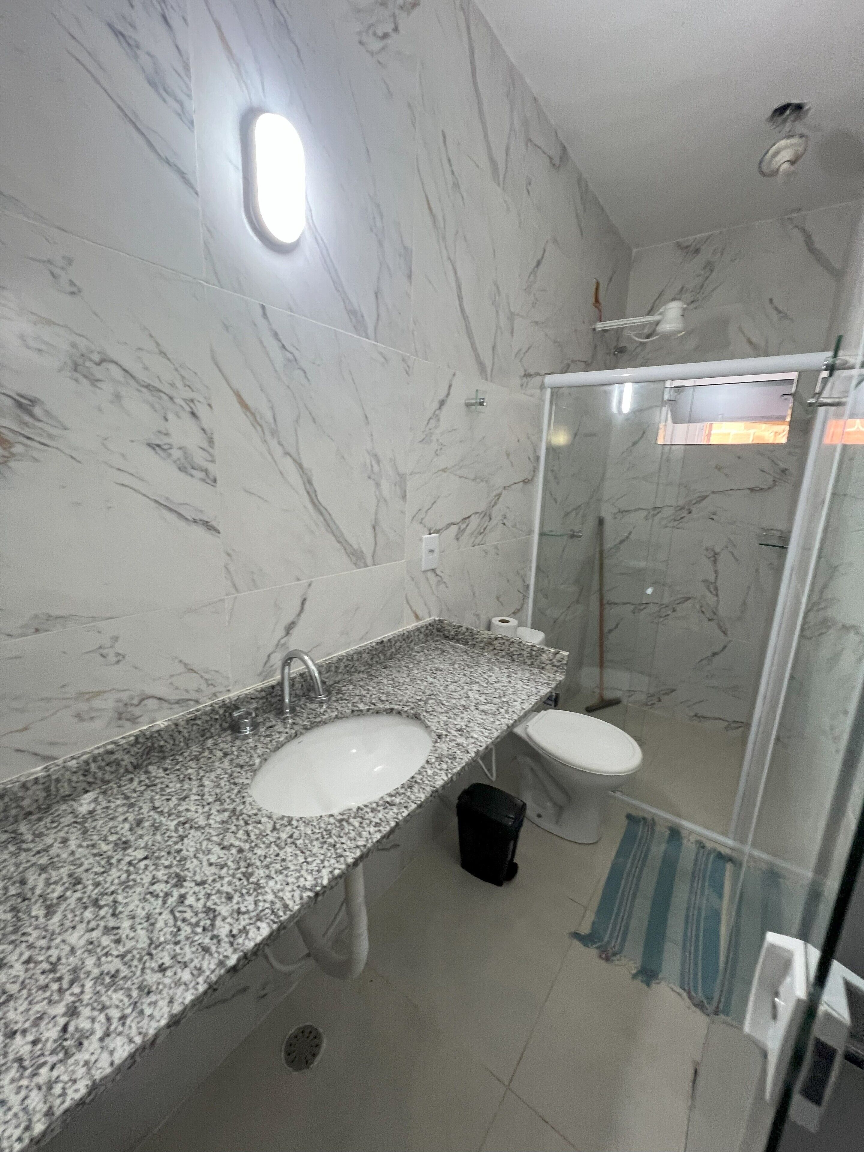 Une salle de bain avec des murs en marbre, un plan de travail en granit, un lavabo, des toilettes et un espace douche.