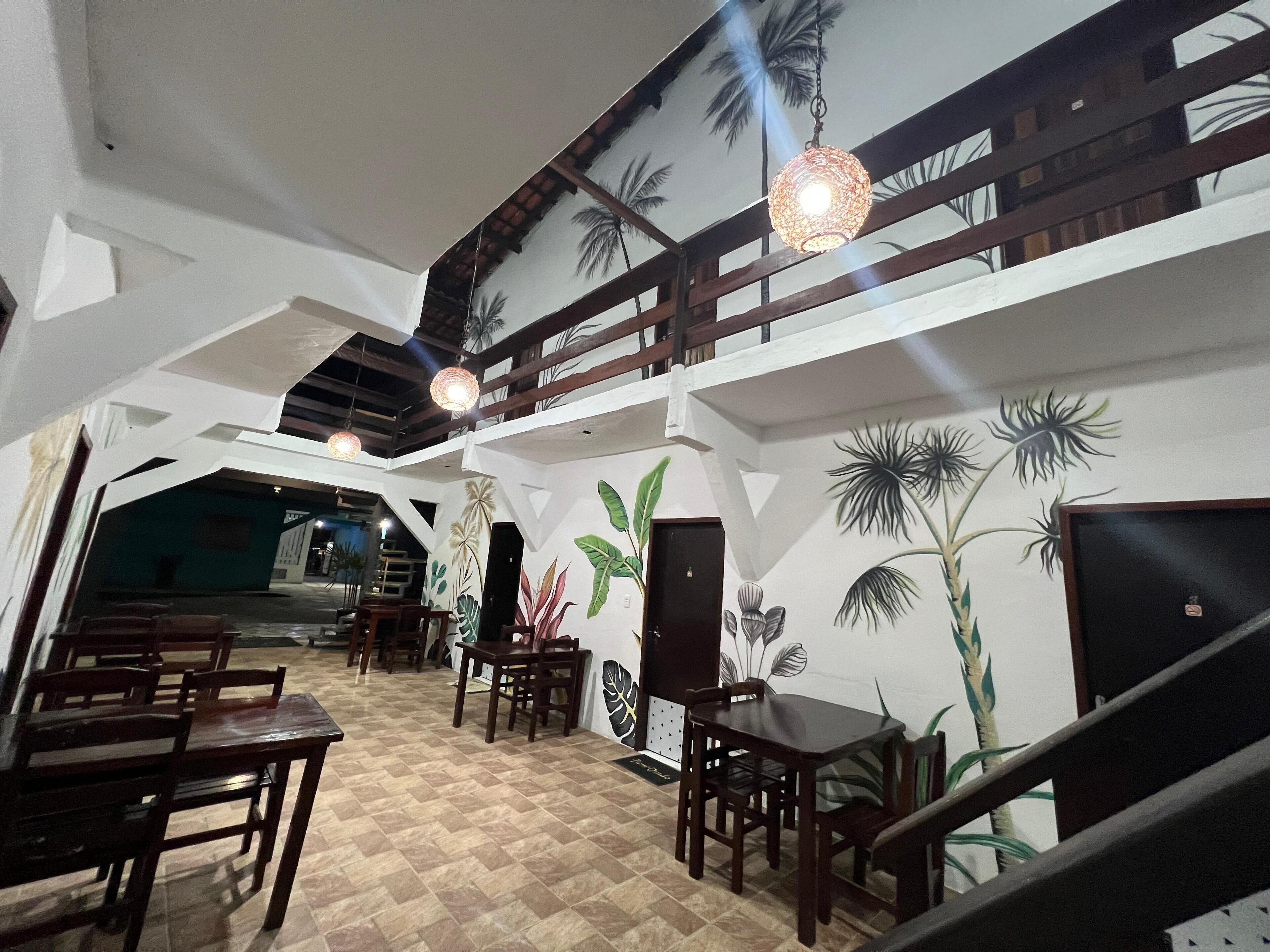 Un restaurant avec des meubles en bois, un sol à carreaux et une fresque représentant des plantes tropicales sur les murs.