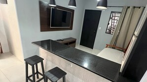 A modern kitchen with a black countertop, three black stools, a TV mounted on the wall, and pendant lights. - Toca do pato hospedagem (Paraty)