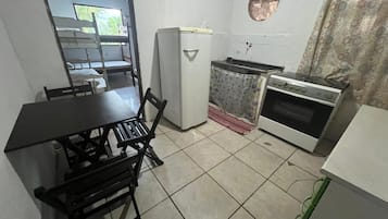 A compact kitchen with a dining table, chairs, a refrigerator, a stove, and a small window.
