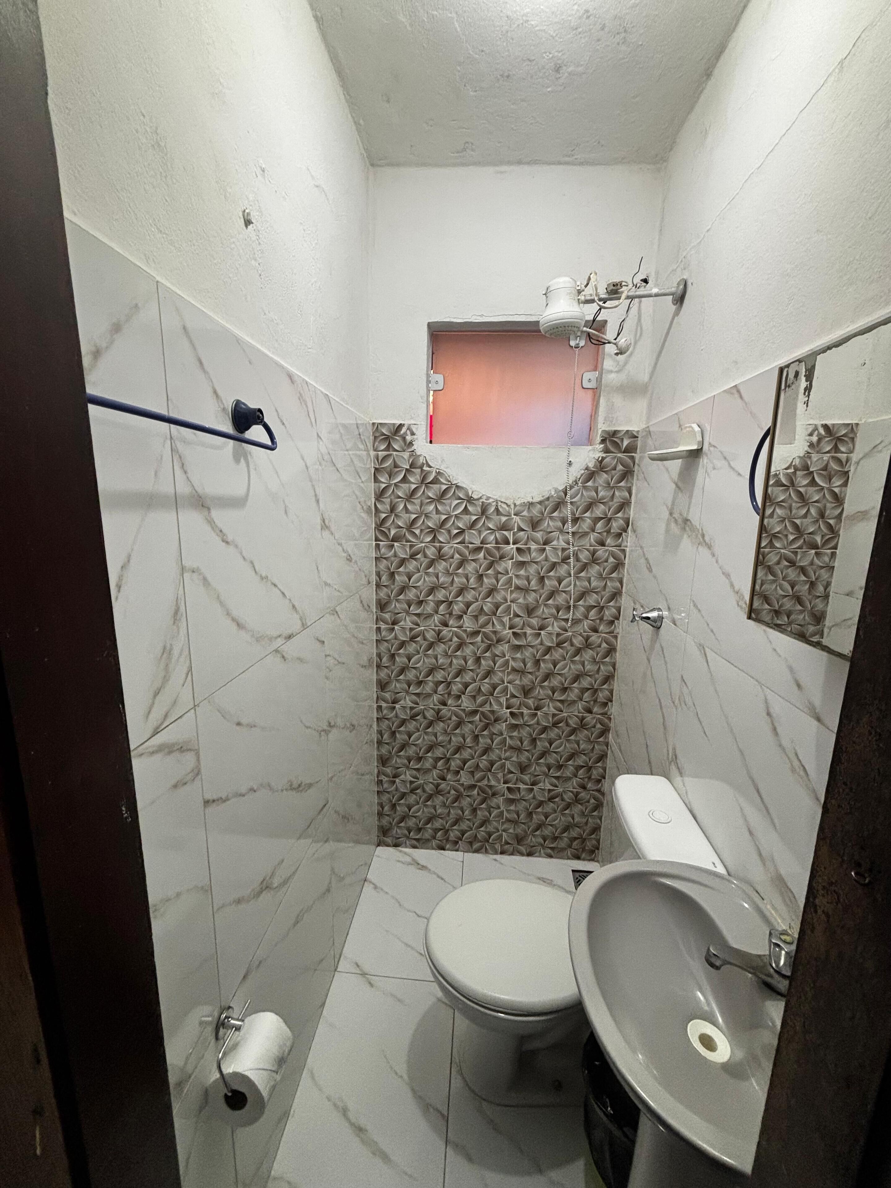 Casa de banho compacta com sanita, lavatório e chuveiro.