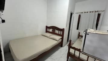 Ein kleines Zimmer mit einem Einzelbett, einem Holz-Kopfteil, einem Holzstuhl und einer weißen Tür mit Spiegel.