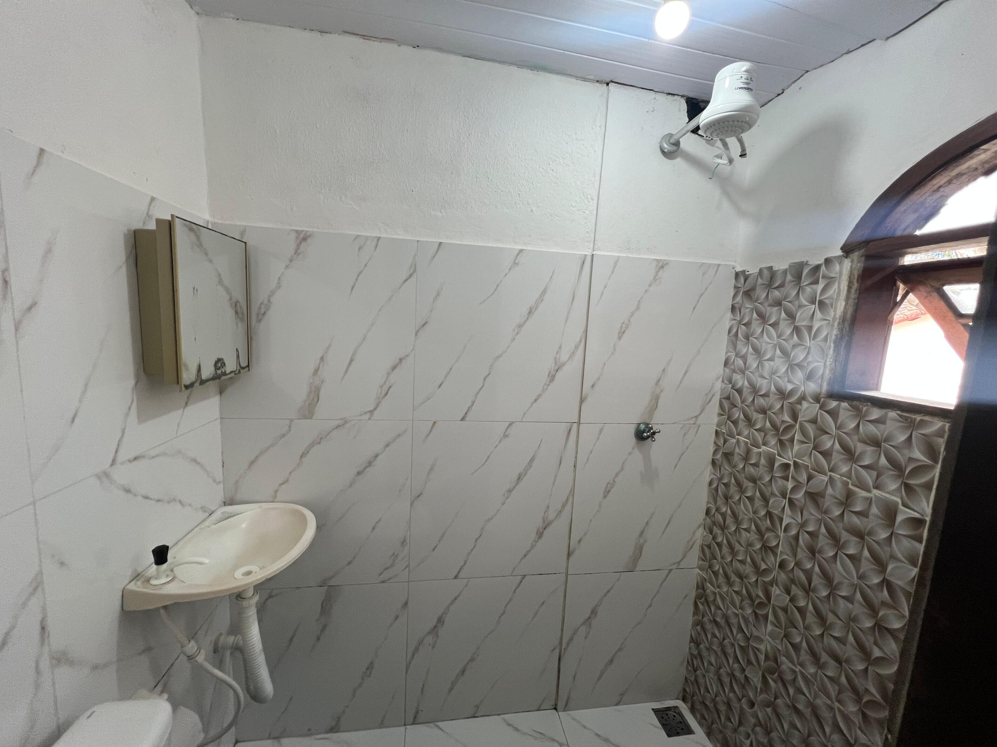 A bathroom with a marble floor, a sink, a mirror, and a shower area with textured walls.
