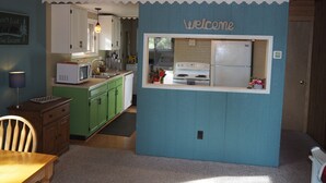 A kitchen with green cabinets, a white refrigerator, and a 'Welcome' sign. - The Cub Hill Chalet on Cub Lake - Private Lakefront, Dock, Raft, Water Toys, Huge Deck, and Spa! (Kalkaska)