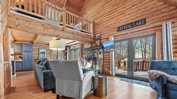 A log cabin interior with a fireplace, a balcony, and a view of Crystal Lake. - The Hillside Hideaway at Crystal Lake - Gorgeous with Great Outdoor Deck and Spa! (Beulah)