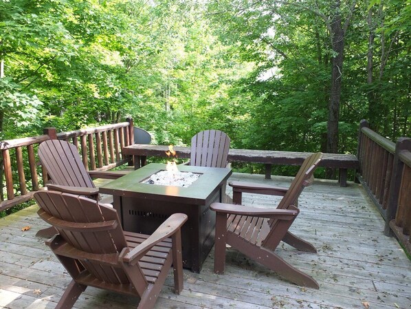 Una terraza de madera con una mesa cuadrada y cuatro sillas tipo Adirondack, rodeada por una barandilla de madera.