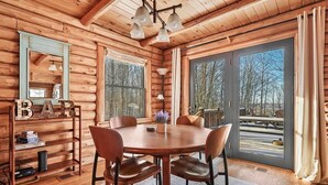 A wooden cabin interior with a round dining table, four chairs, a chandelier, and large windows. - The Hillside Hideaway at Crystal Lake - Gorgeous with Great Outdoor Deck and Spa! (Beulah)