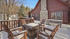 A wooden deck with outdoor furniture, a stone pillar, and a cabin with large windows. - The Hillside Hideaway at Crystal Lake - Gorgeous with Great Outdoor Deck and Spa! (Beulah)