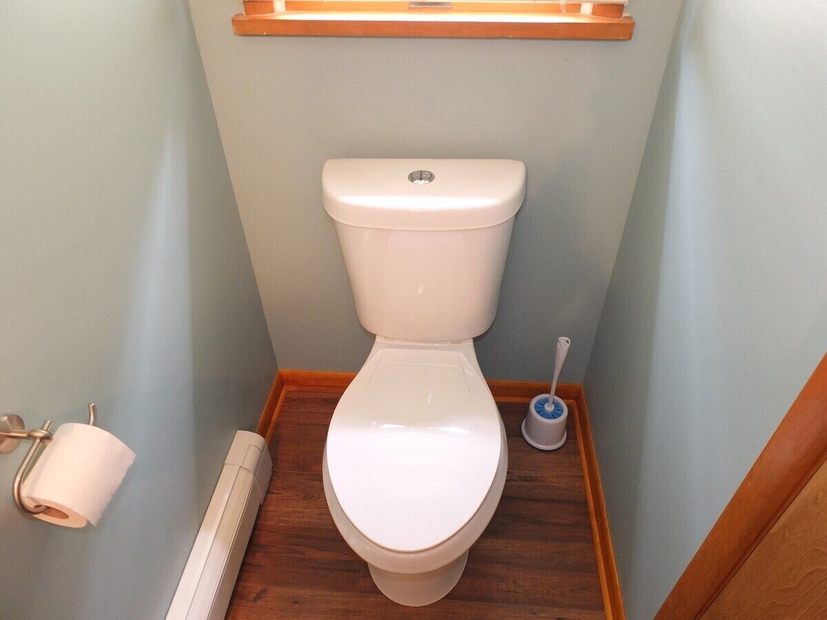 A small bathroom with a white toilet, a toilet paper holder, a hand dryer, and a toilet brush.