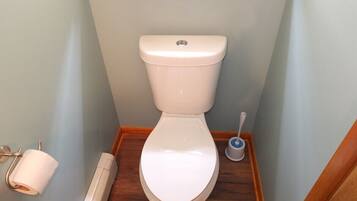 A small bathroom with a white toilet, a toilet paper holder, a hand dryer, and a toilet brush.