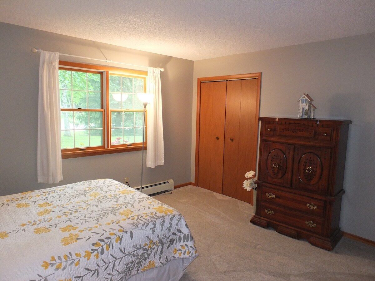 A bedroom with a bed, a dresser, a window with curtains, and a door.