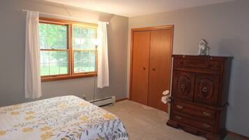 A bedroom with a bed, a dresser, a window with curtains, and a door.