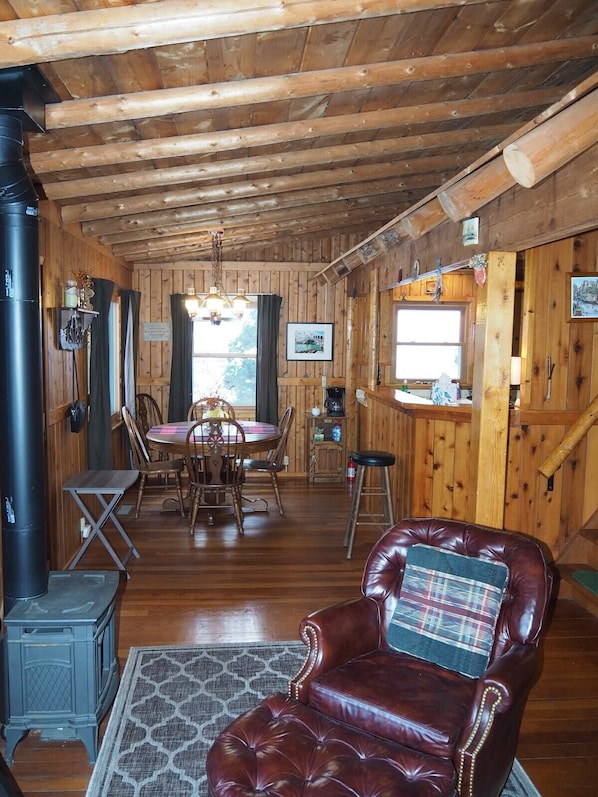 L’intérieur d’un chalet en bois comprend un coin repas, un fauteuil en cuir et un espace cuisine.