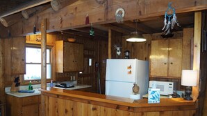 Eine Holzhütte mit einer Küche, die eine zentrale Kochinsel, Holzschränke und eine hängende Leuchte beinhaltet.