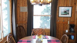 Ein Esszimmer aus Holz mit einem runden Tisch, Stühlen, einer Pendelleuchte, einer Vase mit Zweigen und einem gerahmten Bild an der Wand.