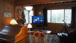 Ein gemütliches Cabin-Interieur mit Holzvertäfelung, einem Klavier, einem Fernseher, einem Weihnachtsbaum und einem Teleskop.
