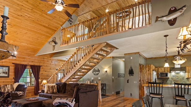 A rustic cabin interior with a wooden staircase, a dining area, and a kitchen with wooden cabinets. - Weatherwood - Gorgeous Luxury Log Cabin with Spa, Sauna, & Games!  8 minutes from Crystal Mountain! (Copemish)