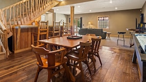 A spacious living area with a wooden staircase, a dining table with chairs, a sofa, and a bar area. - Weatherwood - Gorgeous Luxury Log Cabin with Spa, Sauna, & Games!  8 minutes from Crystal Mountain! (Copemish)