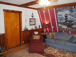 A cozy living room with a wooden door, a red and white striped wall, a blue sofa, a red ottoman, and a patterned rug. - Emanuel - CUTE UPSTAIRS APARTMENT WITH AIR CONDITIONING!  GREAT LOCATION AND DOG-FRIENDLY! (Lake Ann)