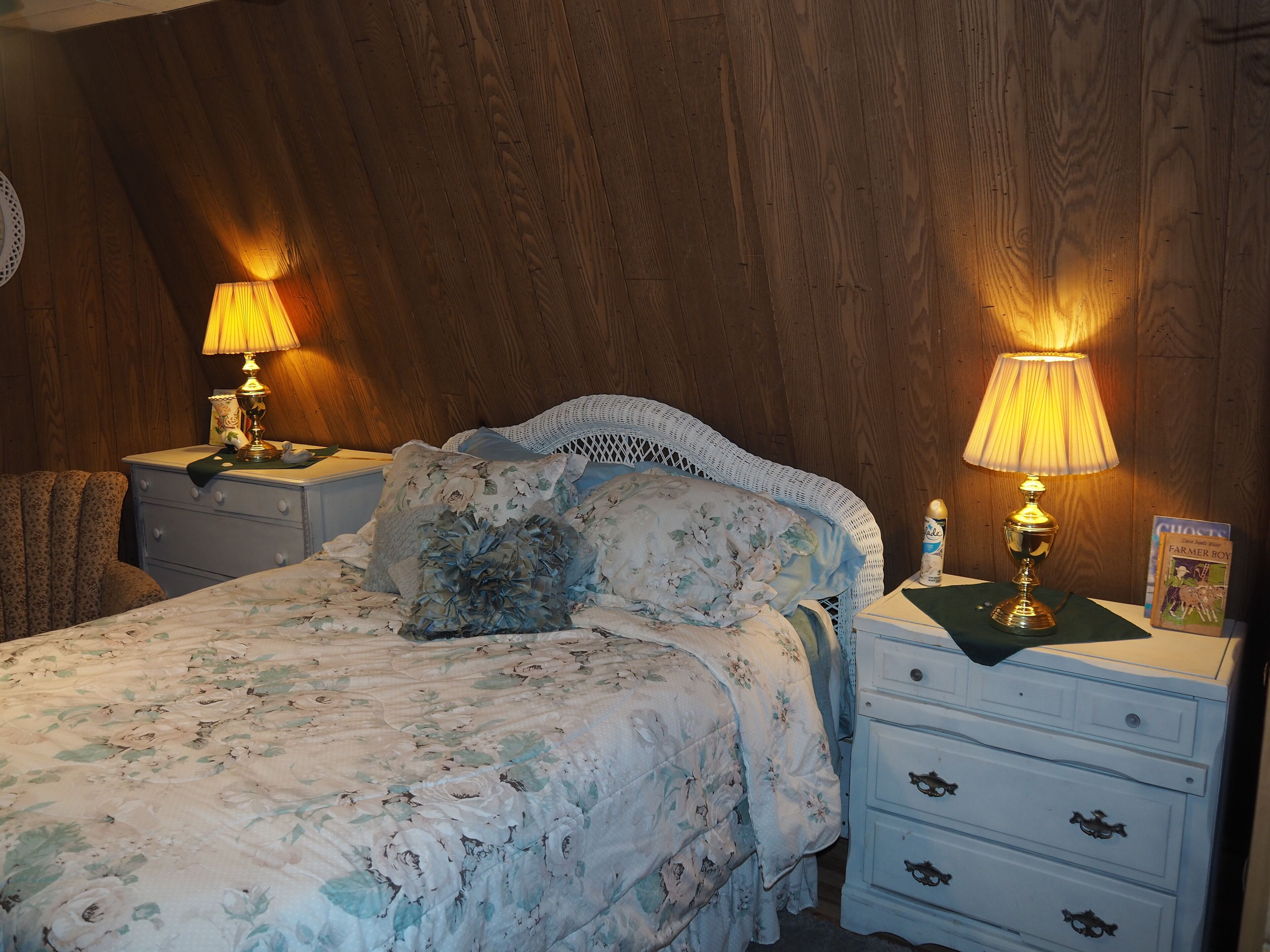 A bedroom with a floral bedspread, two bedside lamps, a white dresser with drawers, and a wooden headboard.