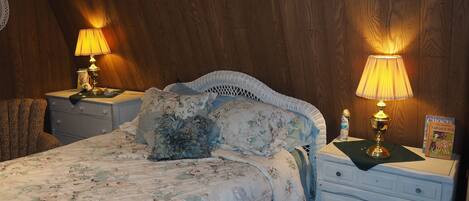 A bedroom with a floral bedspread, two bedside lamps, a white dresser with drawers, and a wooden headboard.