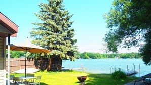 Eine Terrasse mit Tisch und Stühlen, einem Grill und Blick auf einen See.