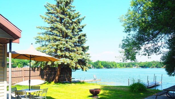 Eine Terrasse mit Tisch und Stühlen, einem Grill und Blick auf einen See.