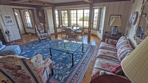 A spacious living room with a large window, a dining area with a table and chairs, and a sofa set.