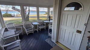 En inglasad veranda med vita flätade stolar och ett litet bord, med utsikt över en sjö och en gräsyta.