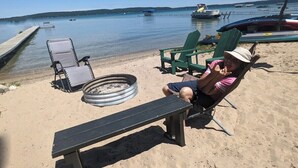 En strand med en bänk, två gröna Adirondack-stolar och en eldstad gjord av ett däck.