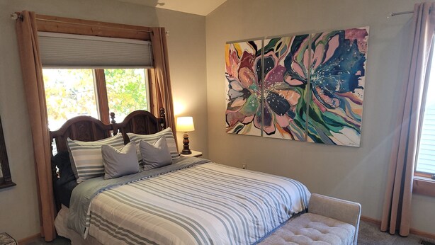 A bedroom with a bed, a bench, a nightstand, a lamp, and a large floral painting on the wall. - The Coral Castle - Large, Newly-Remodeled, Gorgeous, and Great Location!  Walk to Beach and Downtown! (Frankfort)