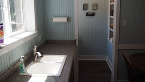 A compact bathroom with a sink, toilet paper, and a small shelf with decorative items. - The Cute & Cozy - Lower Apt. - GREAT LOCATION!  WALK TO DOWNTOWN AND LAKE MICHIGAN! (Frankfort)