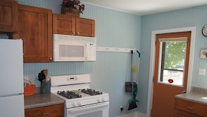A kitchen with wooden cabinets, a white stove, a microwave, and a broom. - The Cute & Cozy - Lower Apt. - GREAT LOCATION!  WALK TO DOWNTOWN AND LAKE MICHIGAN! (Frankfort)