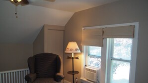Een kamer met een gestreept fauteuil, een staande vloerlamp, een raam met jaloezieën en een airconditioning.