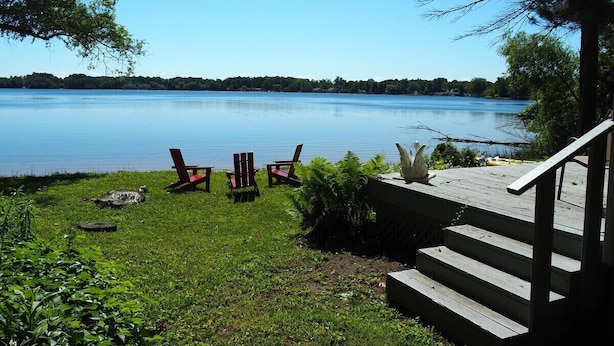 A lakeside deck with outdoor seating and a staircase leading to a building. - A Short's Walk - Sandy Lakefront with Spa / Hot Tub and Kayaks! (Elk Rapids)