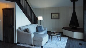 A living room with a grey sofa, a small round table, a lamp, and a fireplace. - A Short's Walk - Sandy Lakefront with Spa / Hot Tub and Kayaks! (Elk Rapids)