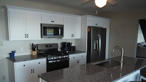 A modern kitchen with white cabinets, a granite countertop, a stainless steel refrigerator, and a built-in microwave. - A Short's Walk - Sandy Lakefront with Spa / Hot Tub and Kayaks! (Elk Rapids)