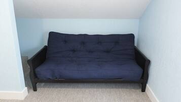 Un canapé bleu foncé se trouve dans un coin d’une pièce aux murs bleu clair et au tapis gris.