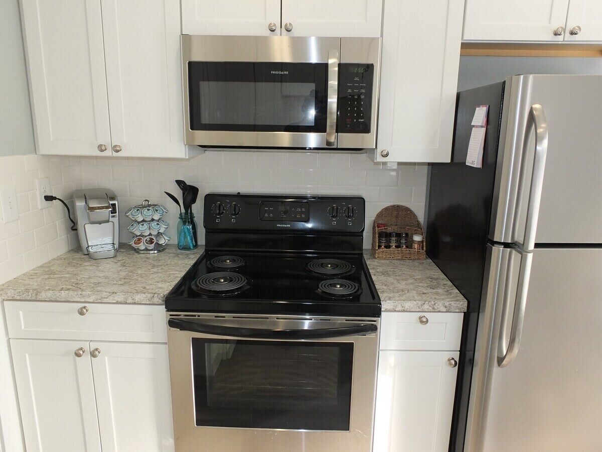 A kitchen with white cabinets, a stainless steel microwave, a black stove, and a refrigerator.