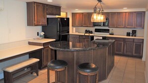 A kitchen with a central island, wooden cabinets, a refrigerator, a microwave, and a coffee maker. - Malabar Cove - LAKEFRONT, QUIET, & RELAXING!  INCLUDES A/C AND KAYAKS! (Gladstone)