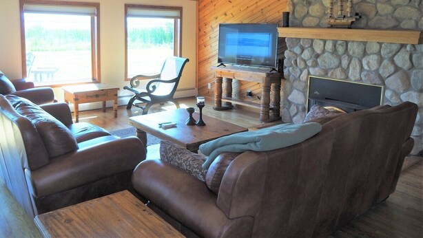 A cozy living room with leather sofas, a stone fireplace, a television, and a wooden ceiling. - Malabar Cove - LAKEFRONT, QUIET, & RELAXING!  INCLUDES A/C AND KAYAKS! (Gladstone)