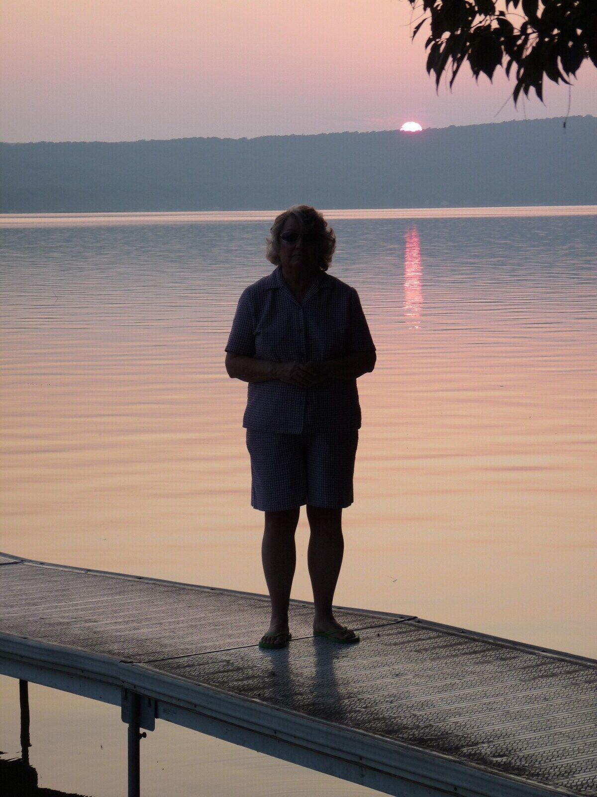 A person standing on a dock with a calm body of water and a sunset in the background.