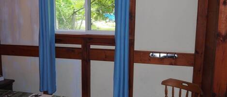 A room with a bed, a wooden chair, a window with blue curtains, and a door.