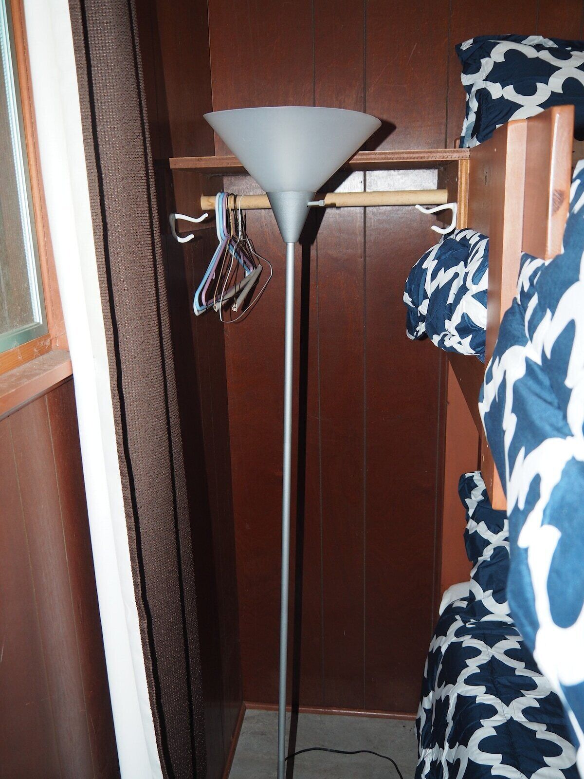 A room with a standing lamp, a wooden wardrobe, and a patterned bedspread.