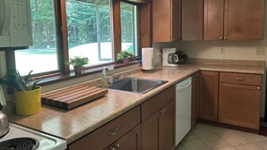 Eine Küche mit Holzausstattung, Spüle, Arbeitsplatte, einer Kaffeemaschine und einem Fenster mit Blick auf Grünflächen.