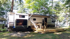 A recreational vehicle with an open kitchen area, a dining table, and a small deck. - Twin Birch Resort - The Loon on the Lake - Lakefront with Dock, Kayak, and Rowboat! (Honor)